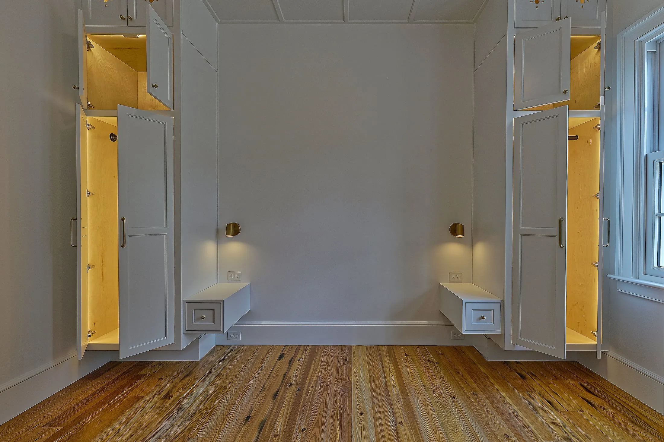 Guest bedroom with a pair of built-in white armoires, doors open to lit interiors, and floating bedside drawers.