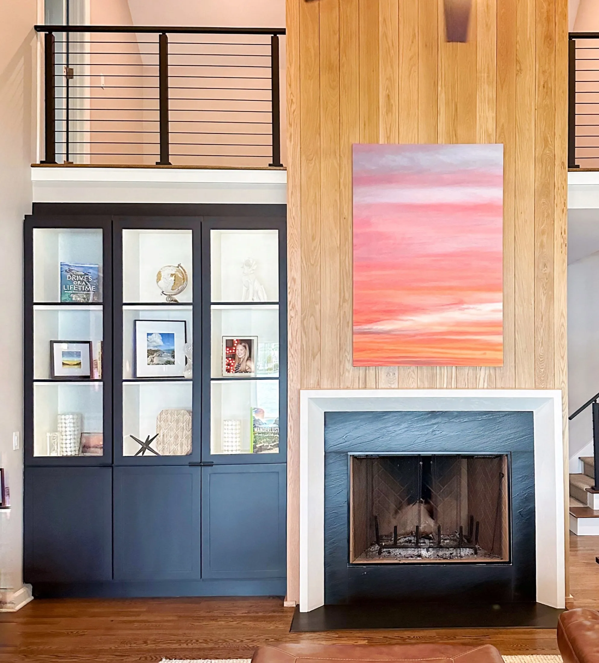 A living room interior with a dark blue bookshelf filled with decorative items and books, a wooden-paneled wall with a pink abstract painting, and a fireplace with a blue and white surround.