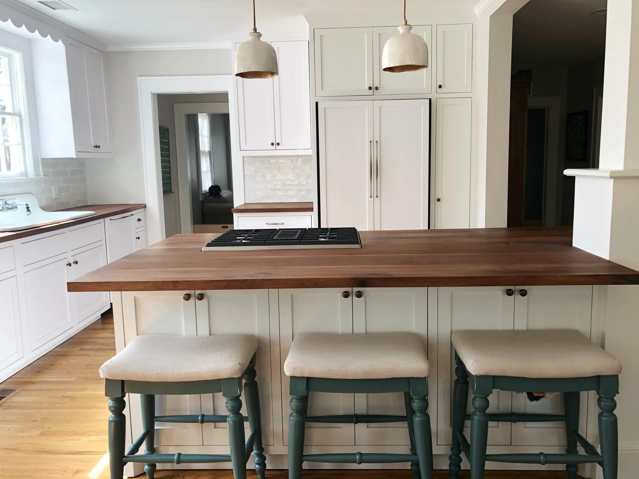 A kitchen with white cabinets, a wooden island with bar stools, and pendant lights hanging from the ceiling.