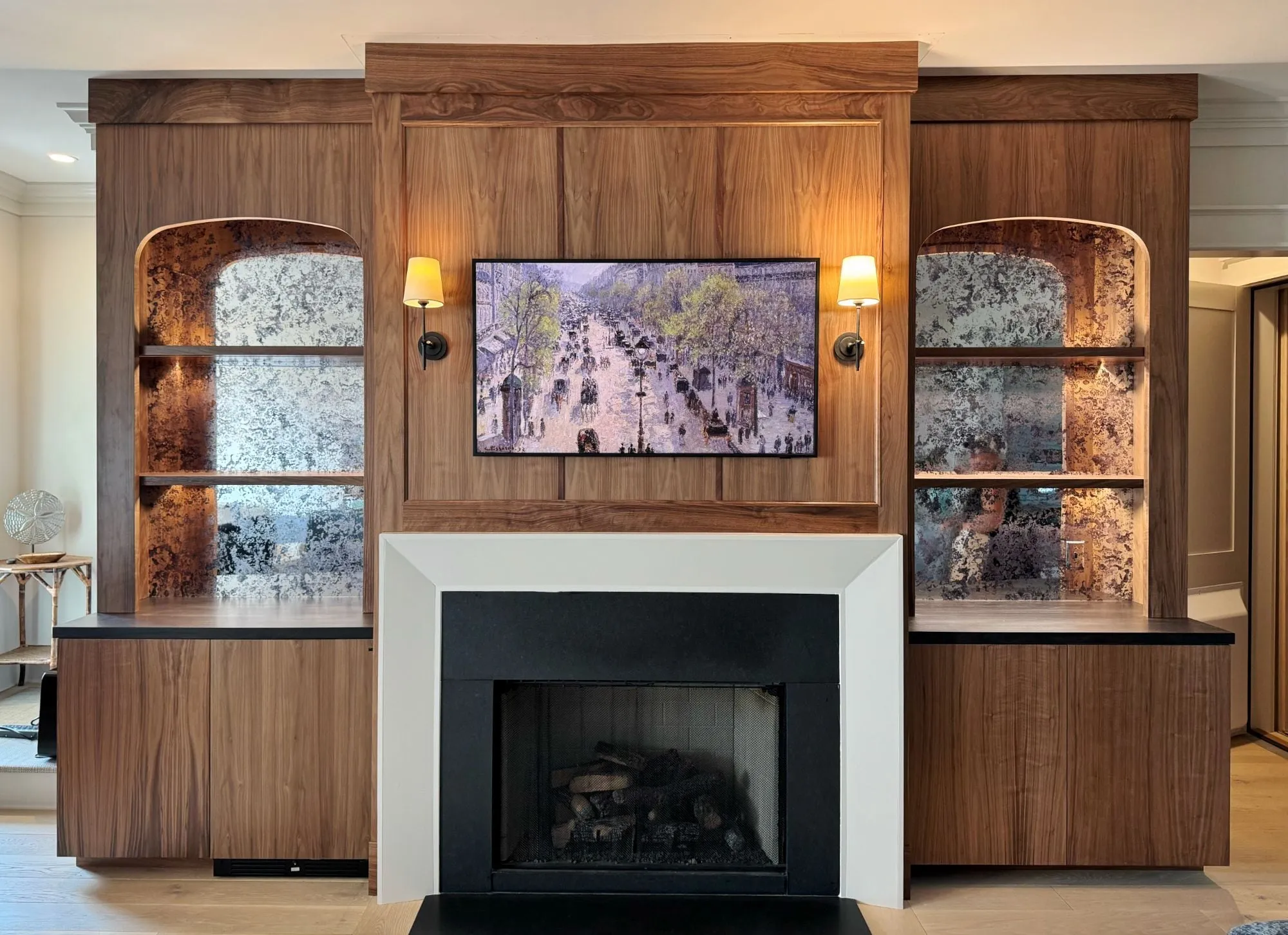 Walnut fireplace wall with arched, lit niches backed in antiqued mirror on either side of a paneled overmantel.