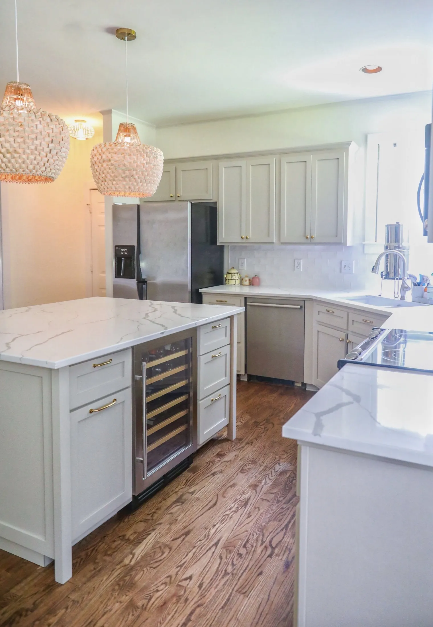 Kitchen with white cabinets, marble countertops, stainless steel refrigerator, and pendant lights.
