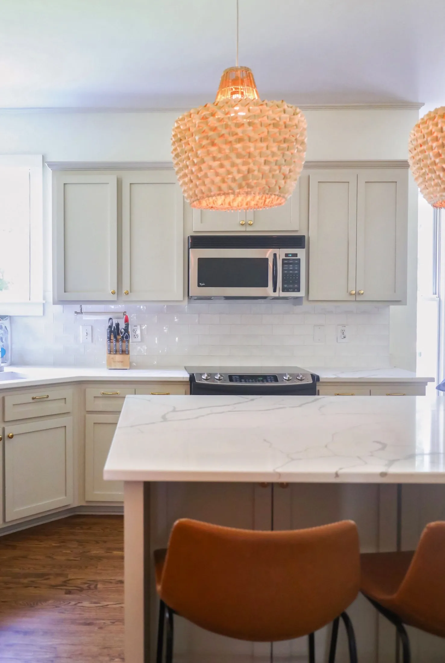 Modern kitchen with white cabinets, marble island, and pendant lights with textured lampshades.