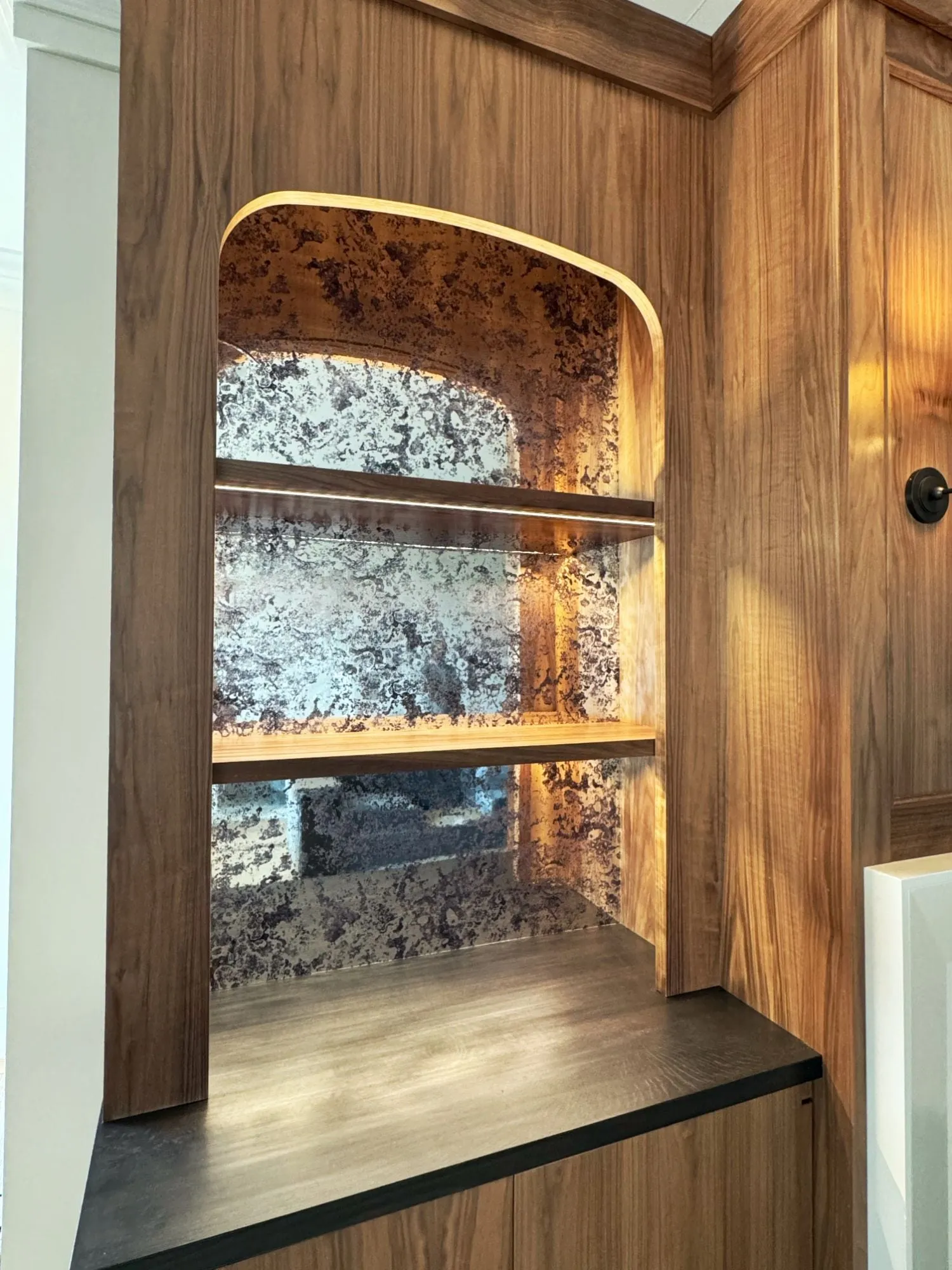 Walnut built-in beside the fireplace: an arched niche with antiqued mirror, lit shelves and a dark oak counter.