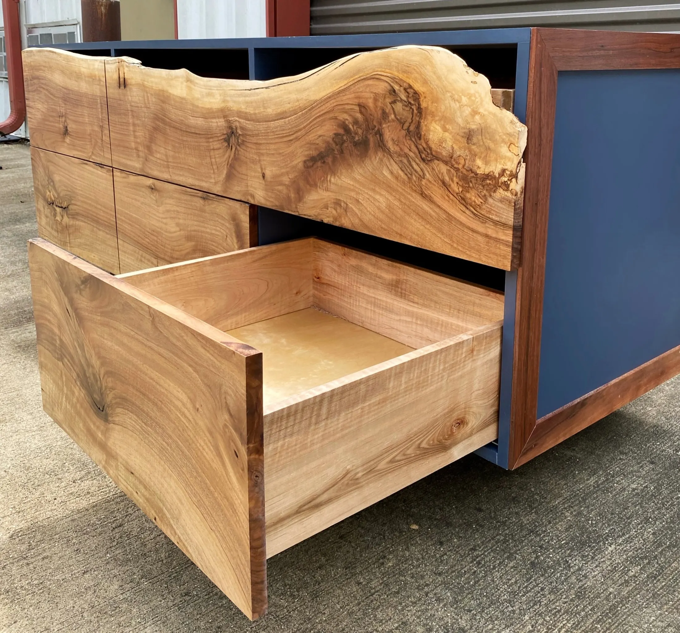 A wooden cabinet with a large, natural wood grain pattern, featuring an open drawer at the bottom and wood panels on the front.