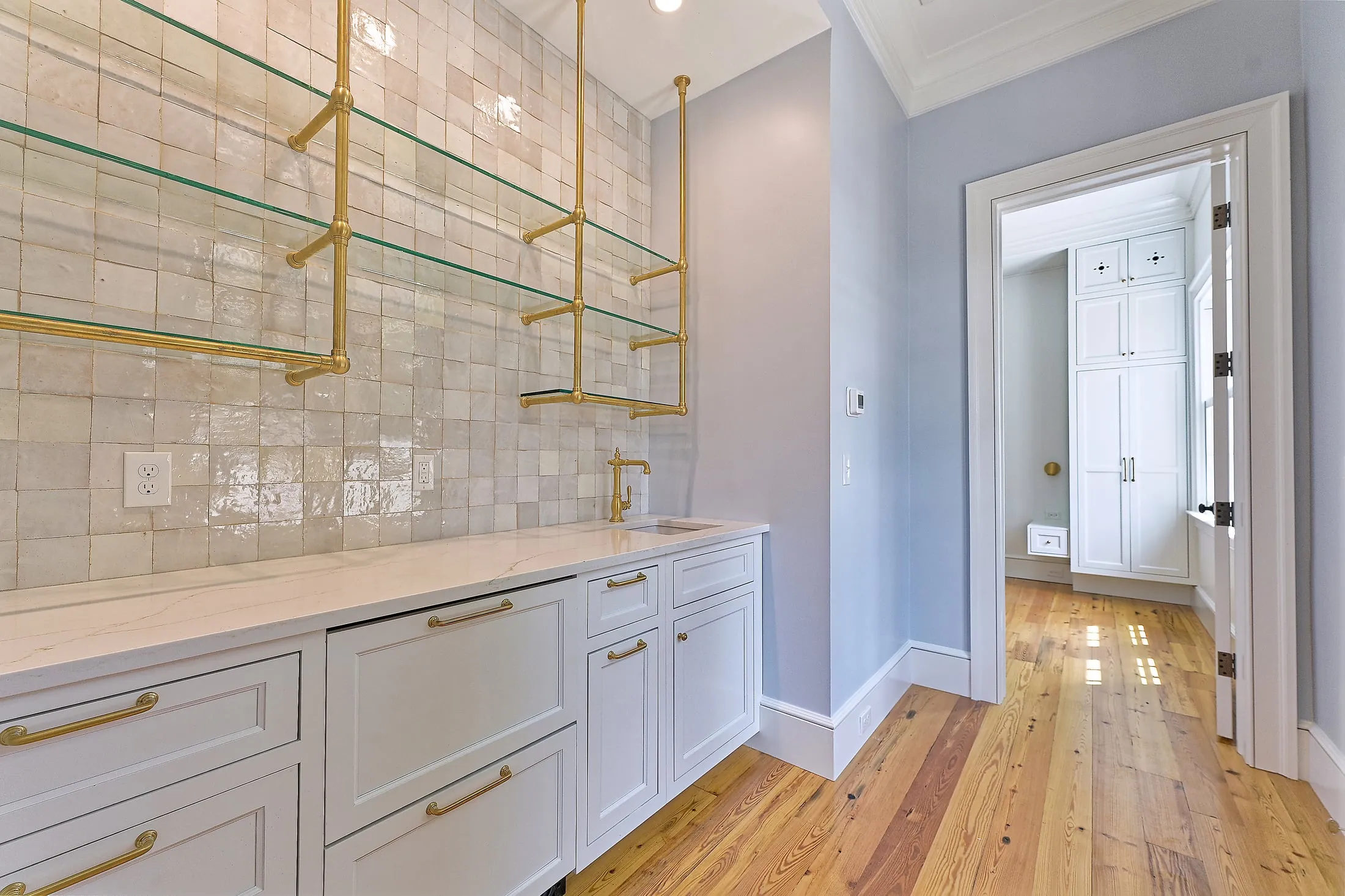Kitchenette with white inset cabinetry, a marble counter, glazed tile and brass open shelving.