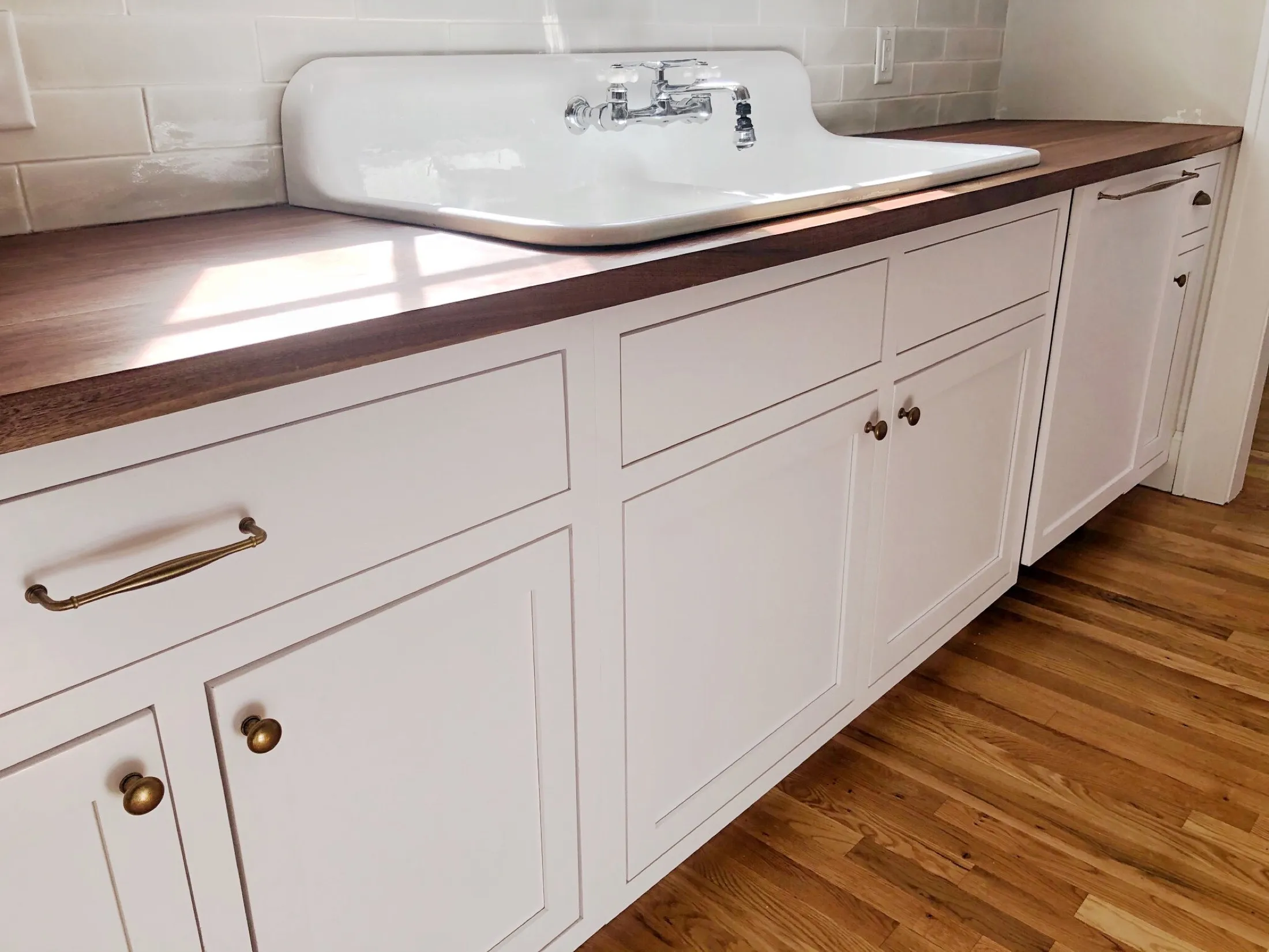 A white countertop with a built-in sink and a silver faucet, set against a white tiled wall, with a wooden floor below.