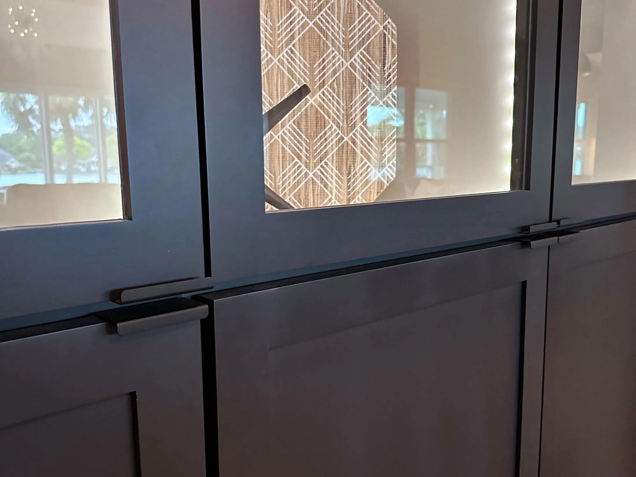 Close-up of black cabinet doors with glass panels showing a patterned object inside, possibly a clock, in a well-lit room.