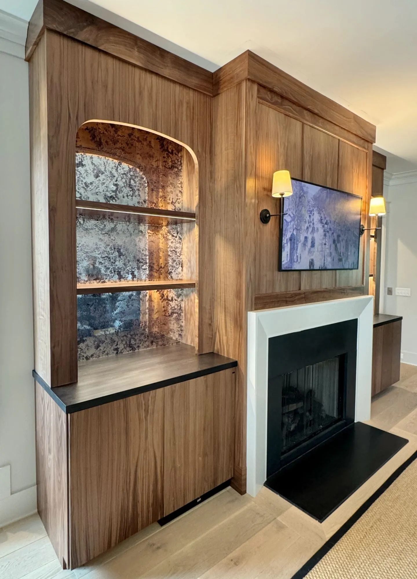 Close-up of an arched walnut niche with antiqued mirror back and lit walnut shelves.