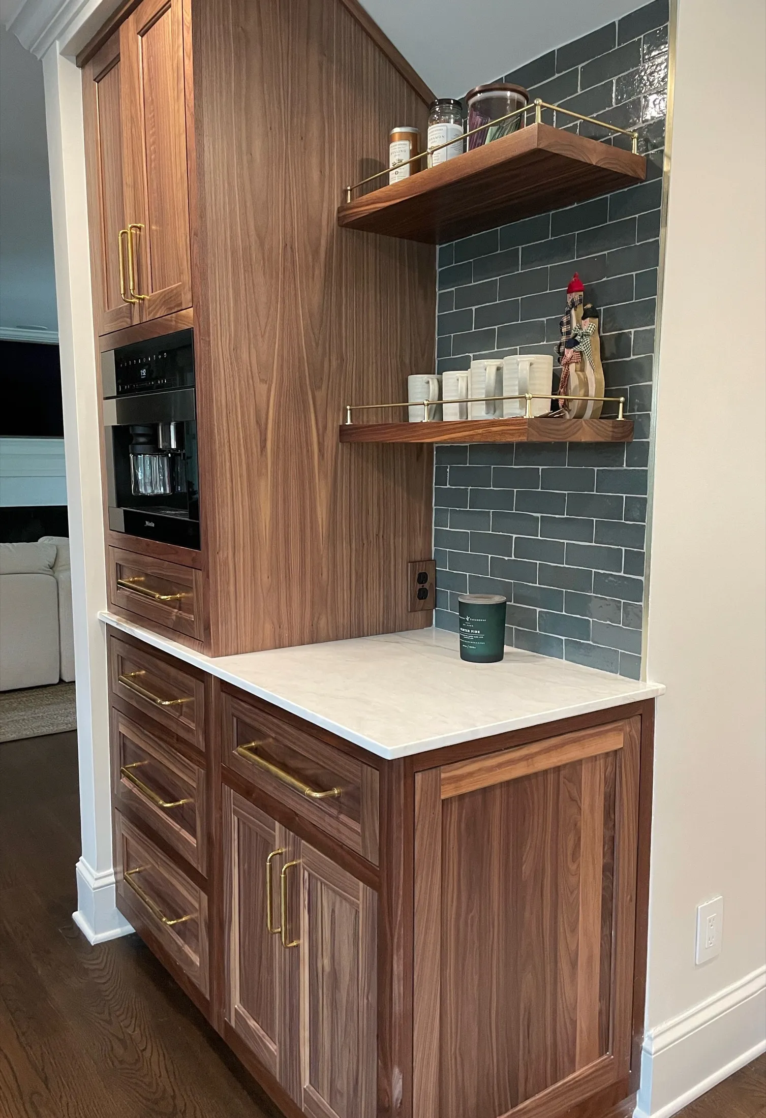 Kitchen corner with wooden cabinetry, black brick backsplash, and open wooden shelves holding jars, cups, and a decorative figurine.