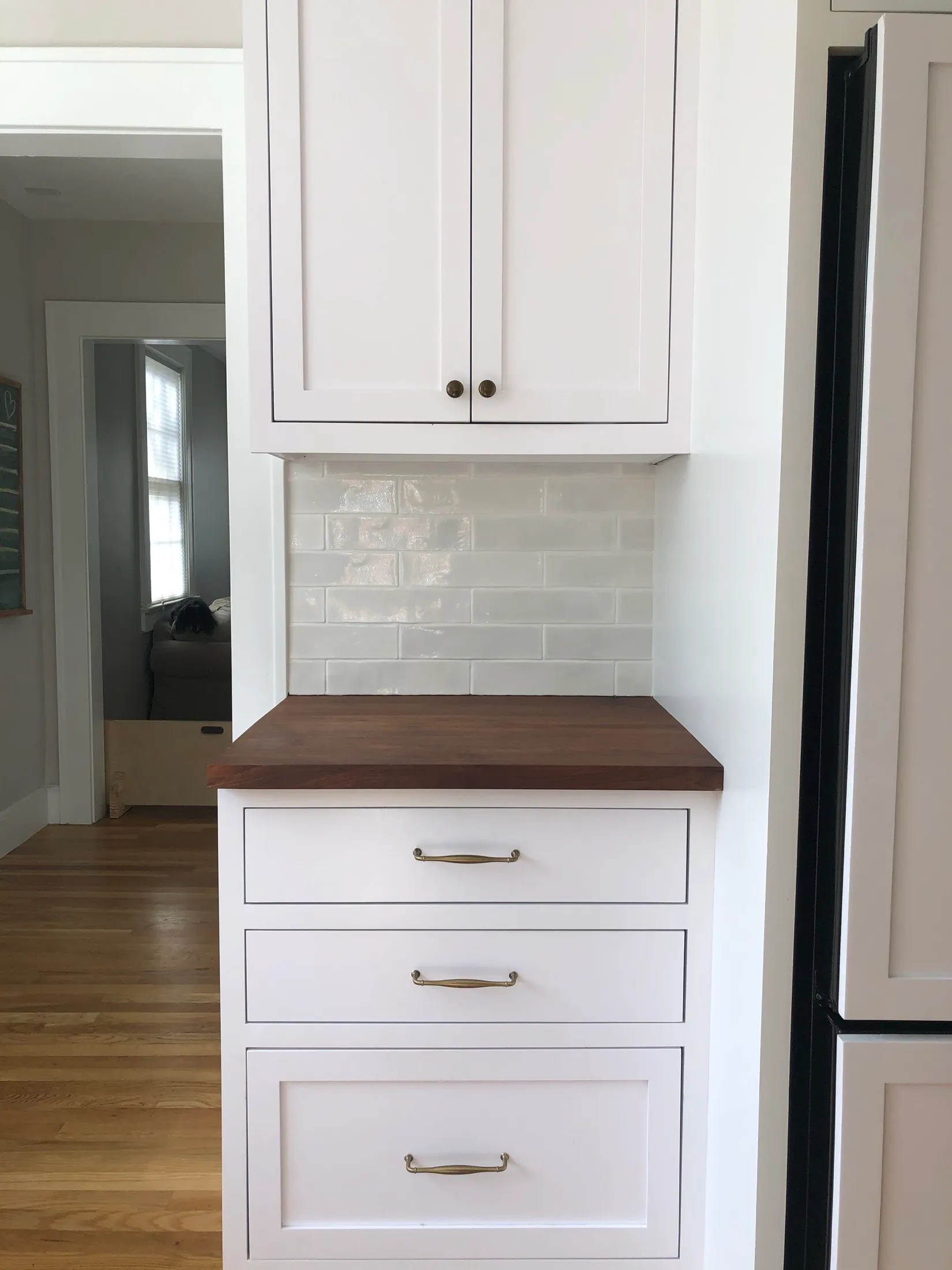 Kitchen with white cabinets, a wooden countertop, beige tile backsplash, and hardwood floors.