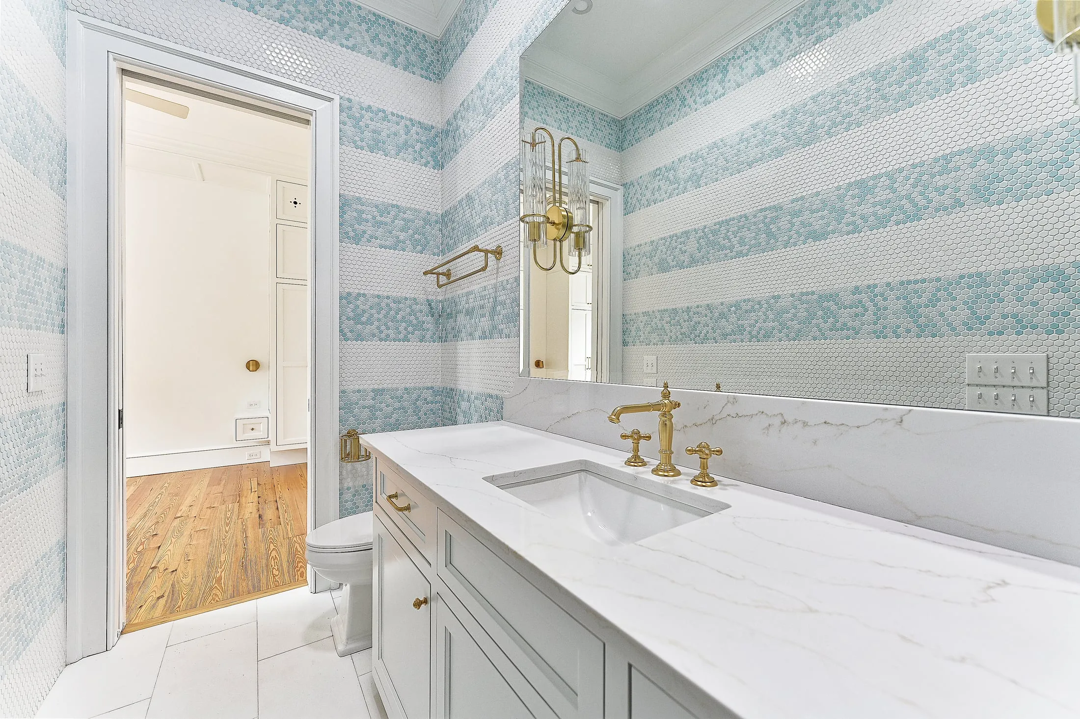 Bathroom vanity in white inset cabinetry with a marble top, brass fixtures and blue striped tile.