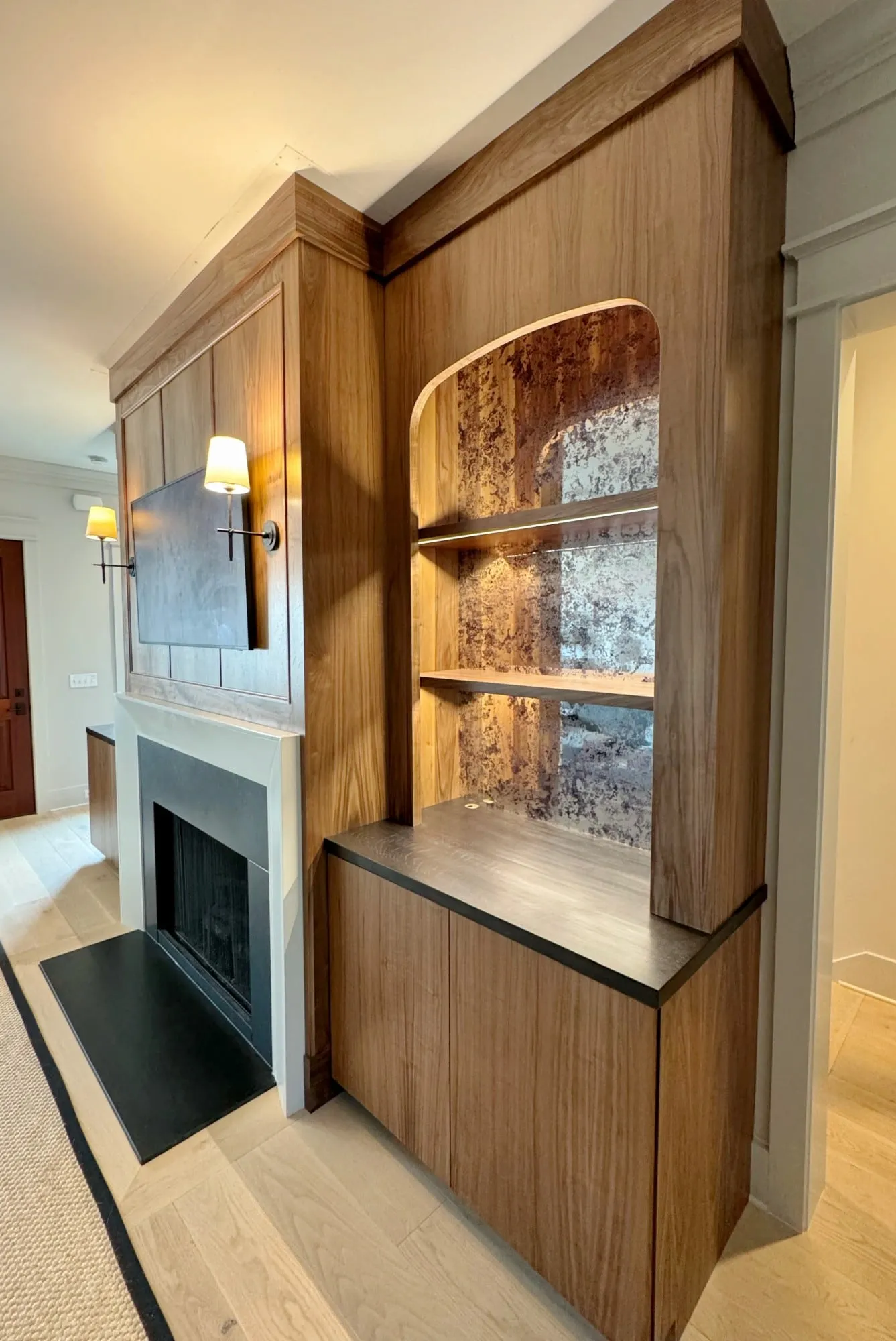 Walnut built-in from the side, showing the arched niche, overmantel paneling and sconce.