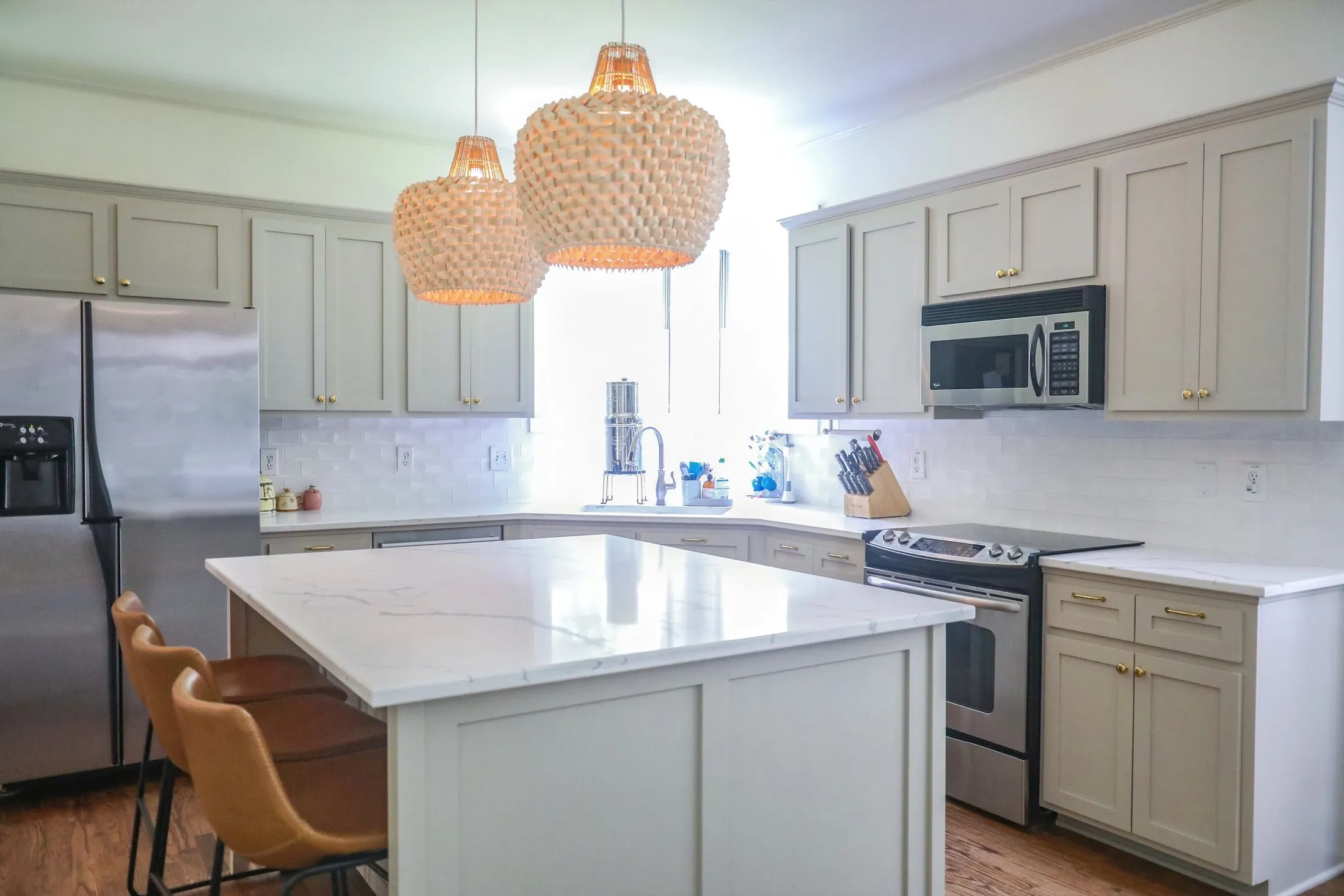 Modern kitchen with white cabinets, marble island, stainless steel appliances, and woven pendant lights.