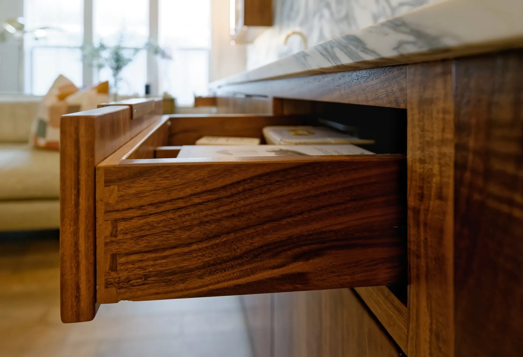 Open walnut drawer showing hand-cut dovetail joinery beneath a marble countertop.