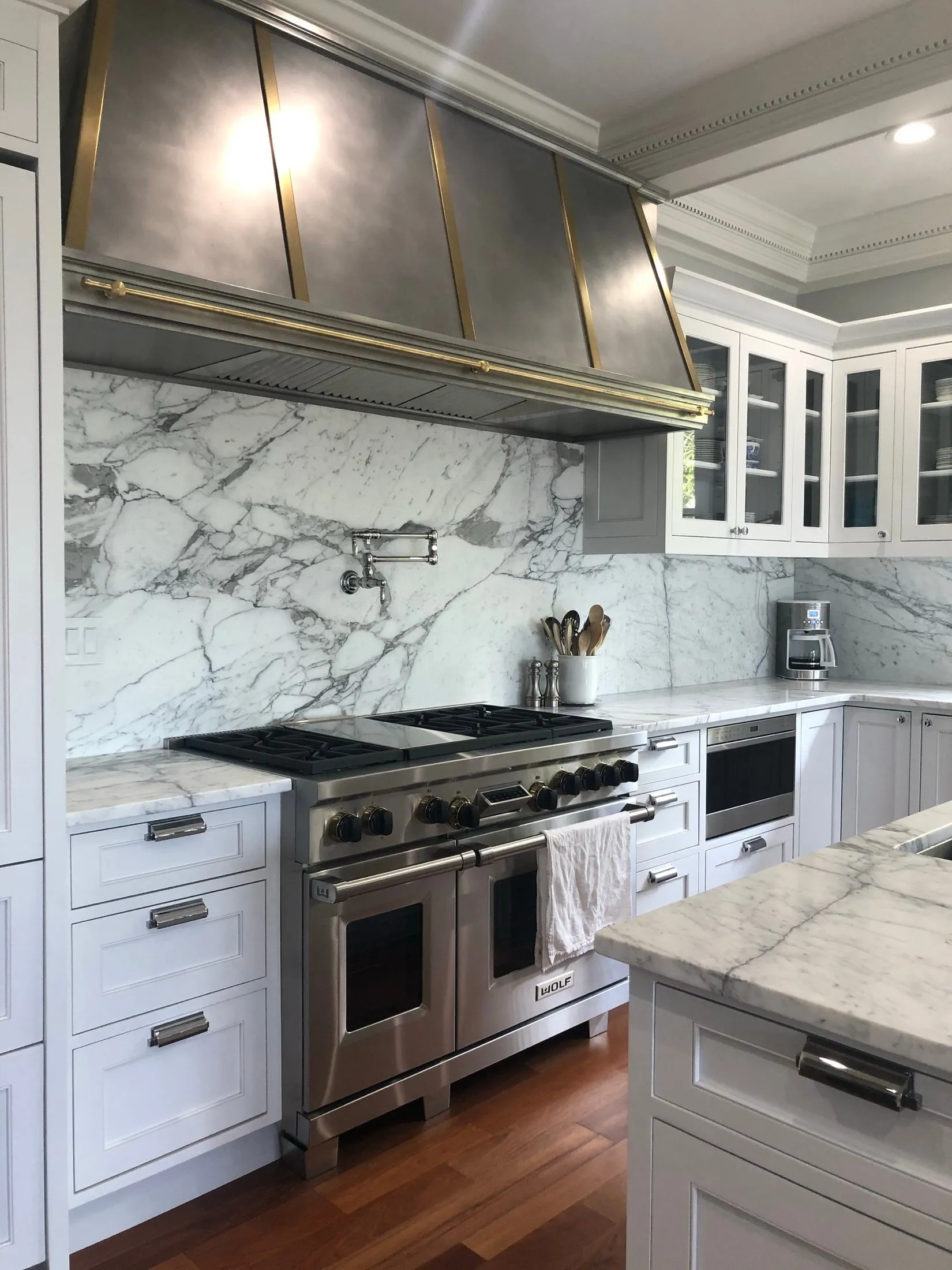 Modern kitchen with white cabinetry, marble countertops, stainless steel appliances including a range and oven, and a wood floor.