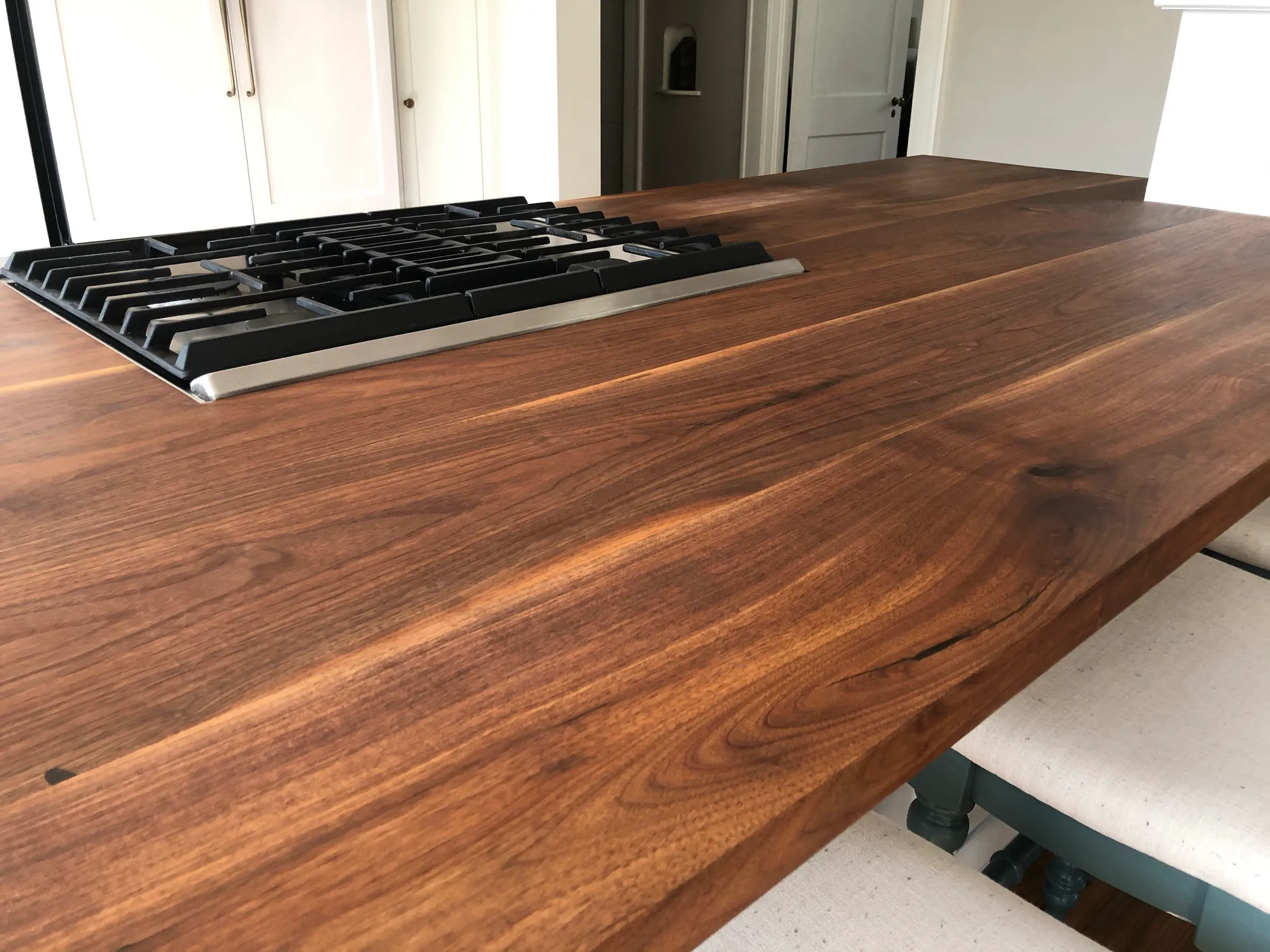 Close-up of a wooden kitchen island with a built-in black stovetop, in a bright room with white cabinets in the background.