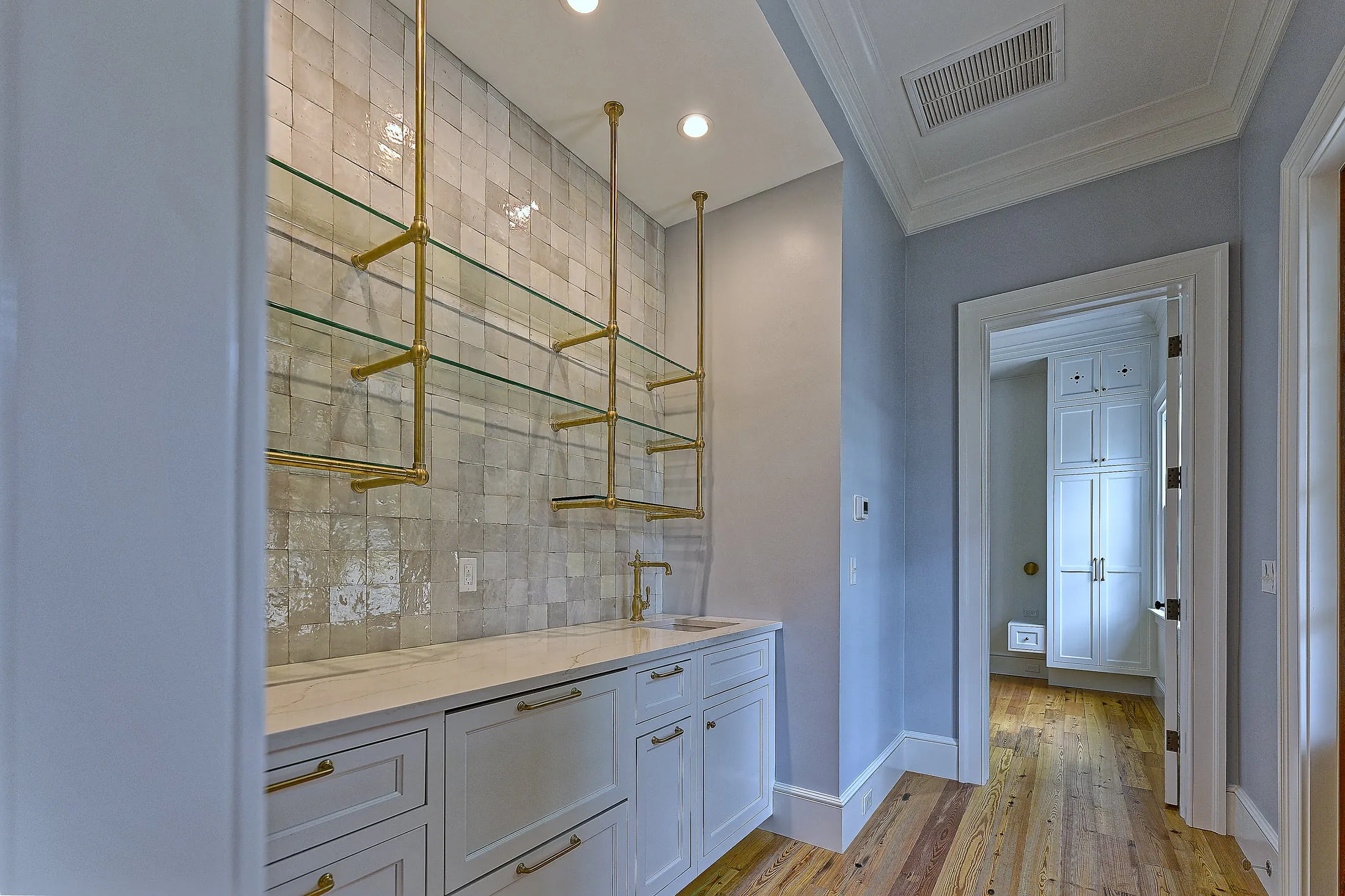 Kitchenette with brass shelving and white cabinetry, looking through to the bedroom.
