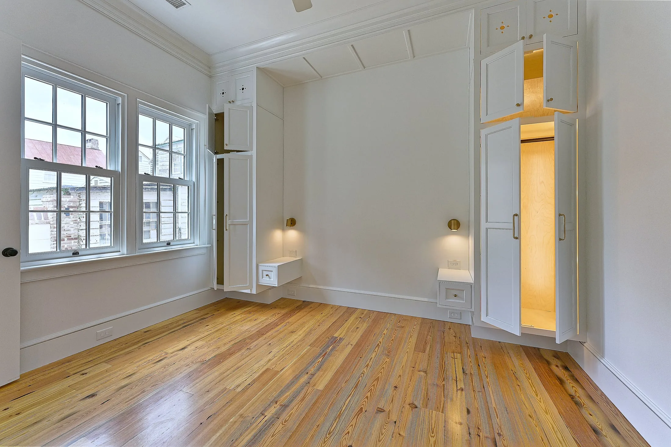 Guest bedroom with built-in armoires and floating bedside drawers between two windows.