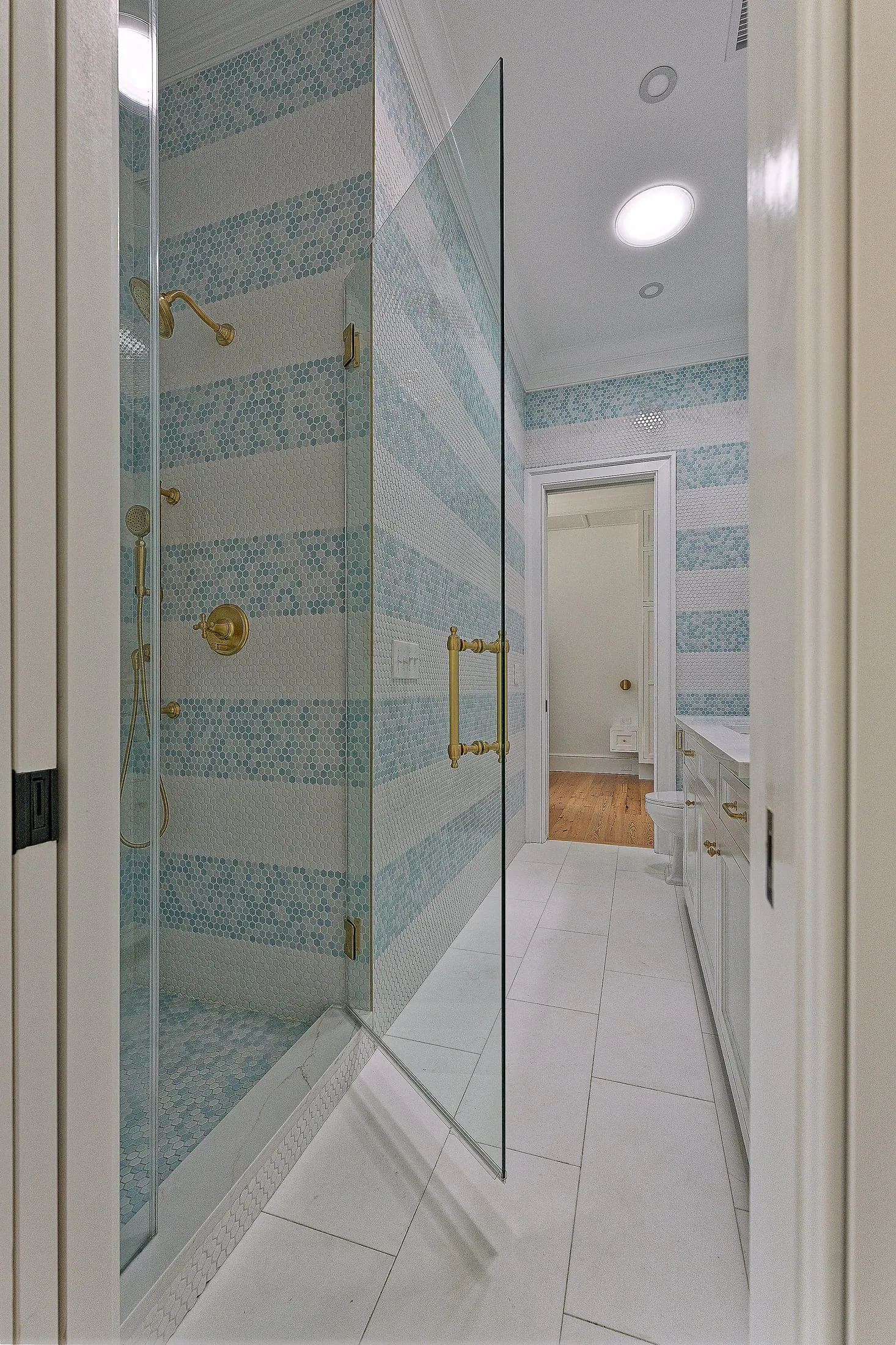 Glass shower and vanity in a bathroom lined with blue striped tile.