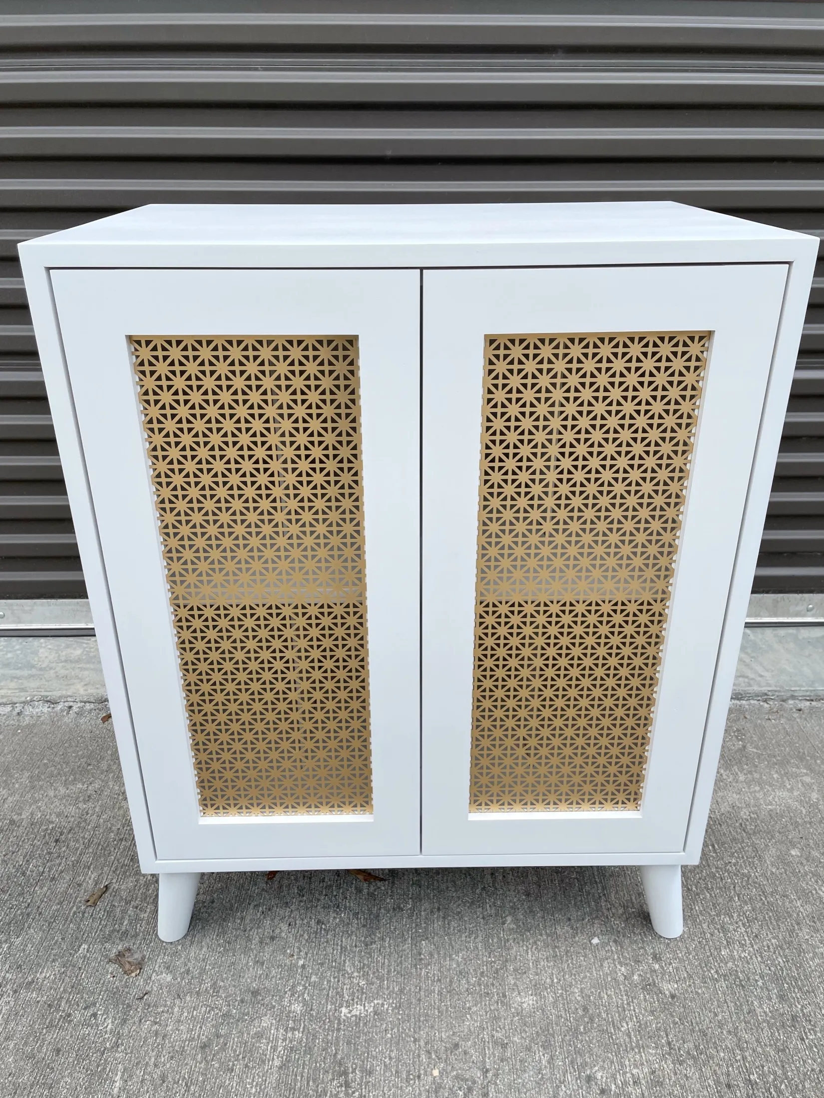 White cabinet with two doors featuring geometric cutouts on a concrete surface.