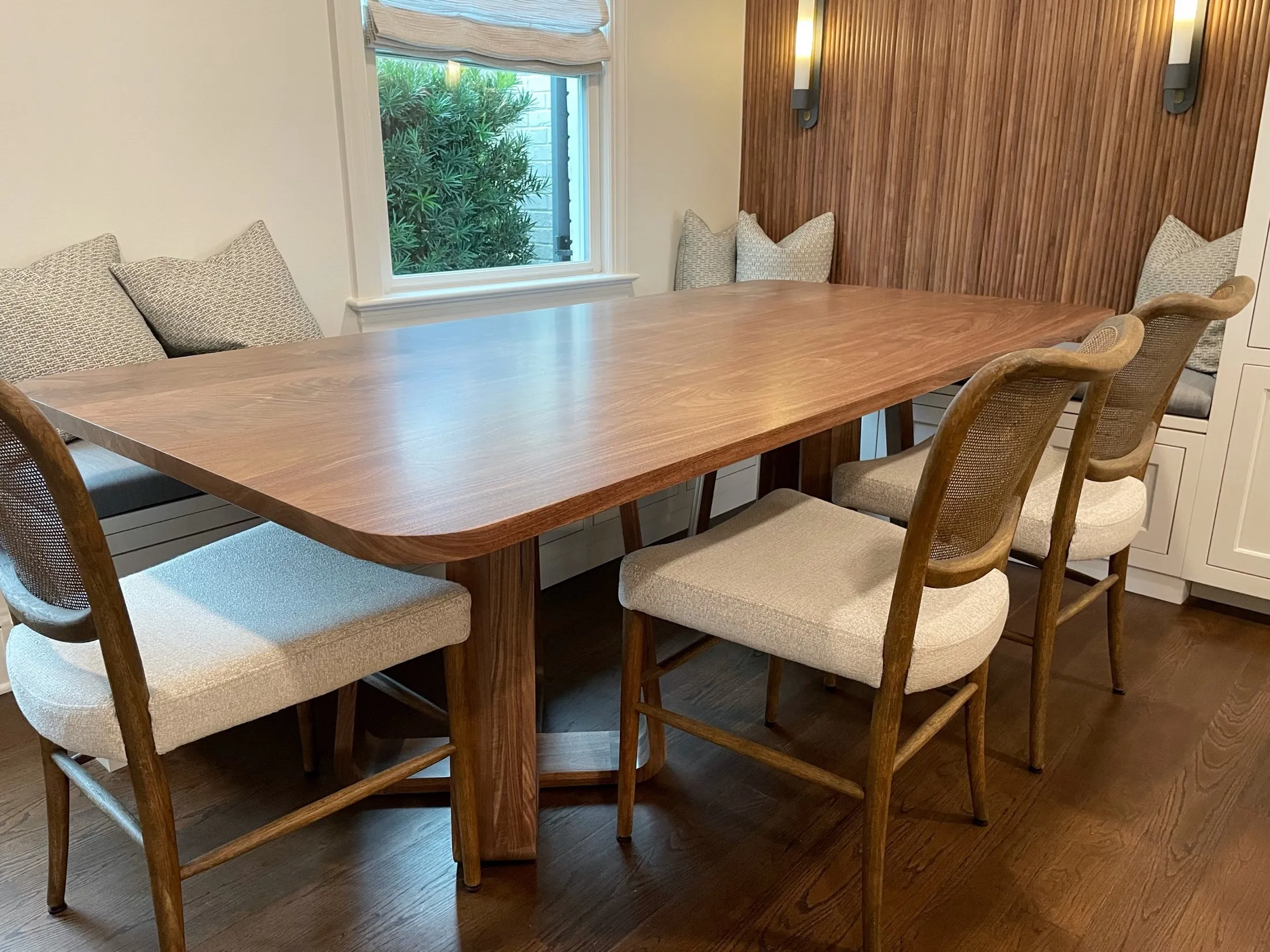 Wood dining table with six chairs, pillows on a bench and window with blinds in a dining room.