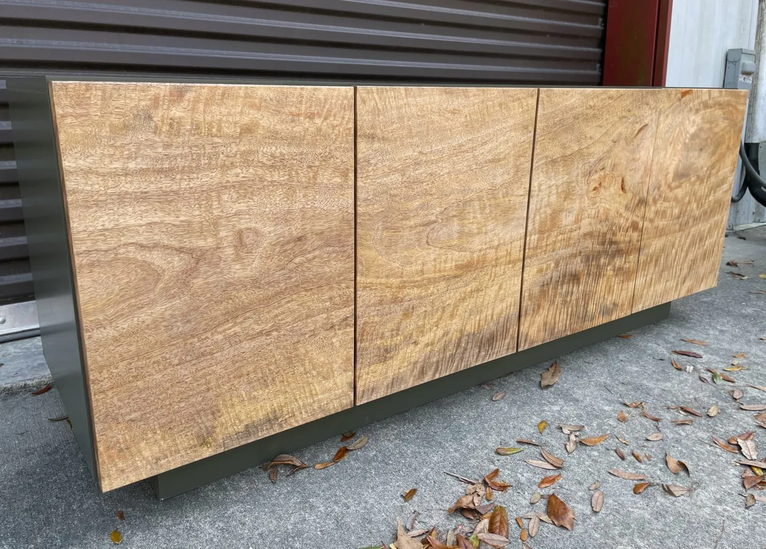 Sideboard with four figured mango wood doors on a sage-green lacquered case, seen at an angle.