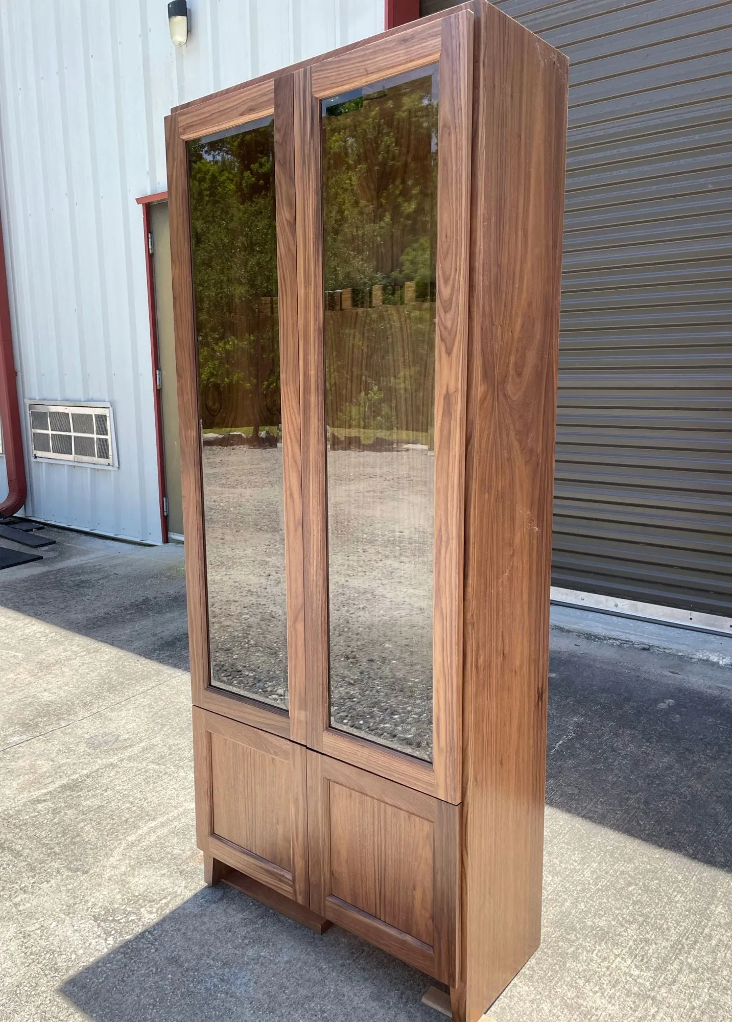 Tall walnut gun cabinet with two glass doors above and two paneled doors below.