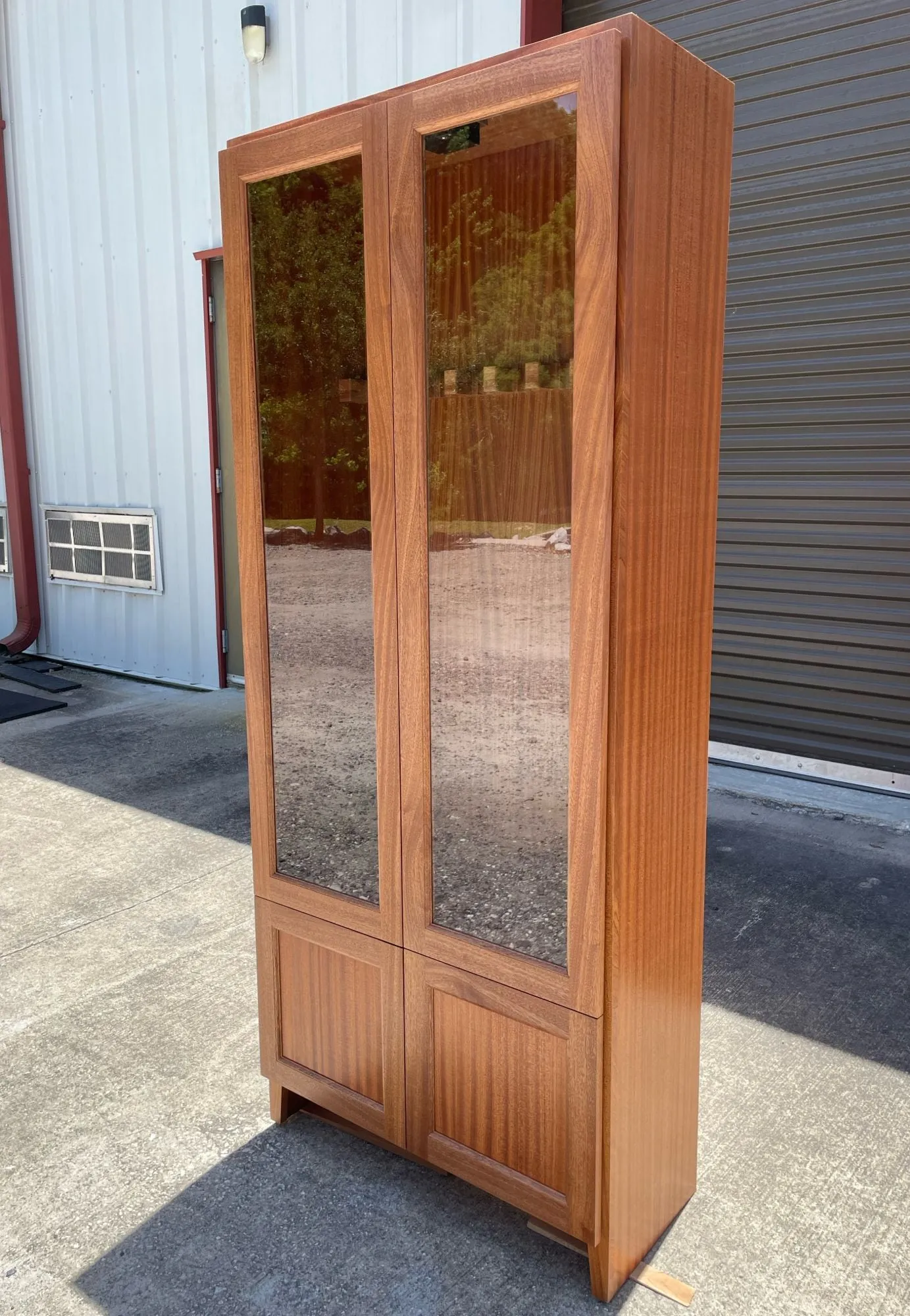 Tall mahogany gun cabinet with two glass doors above and two paneled doors below.